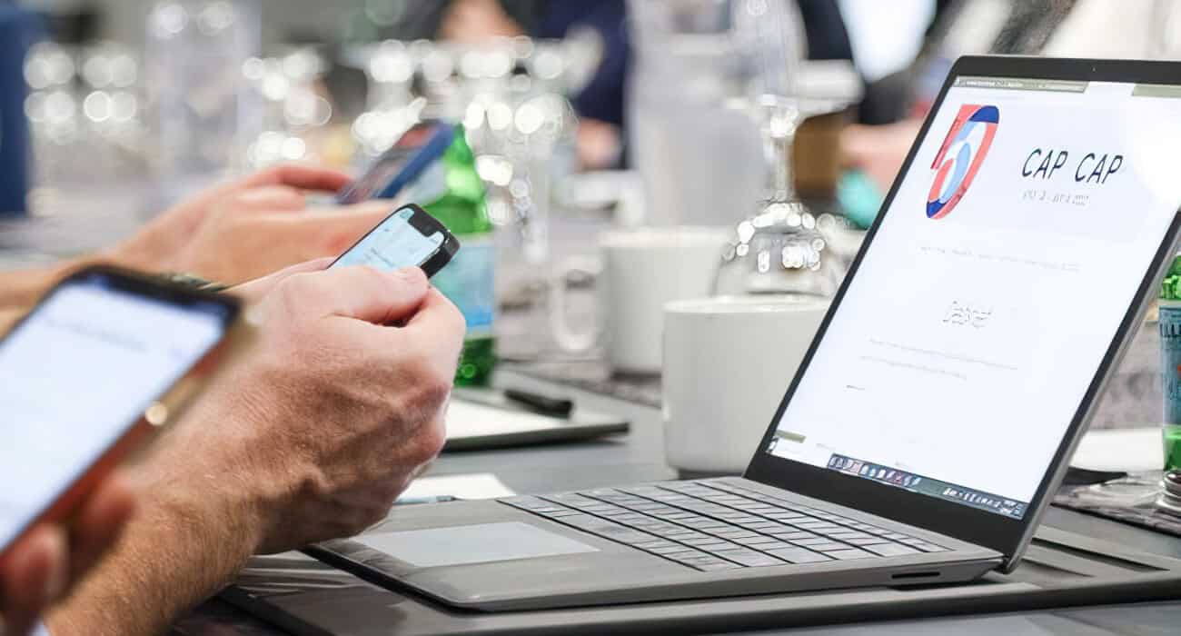 Man holding mobile device while browsing the Metro Chamber Cap to Cap website on laptop